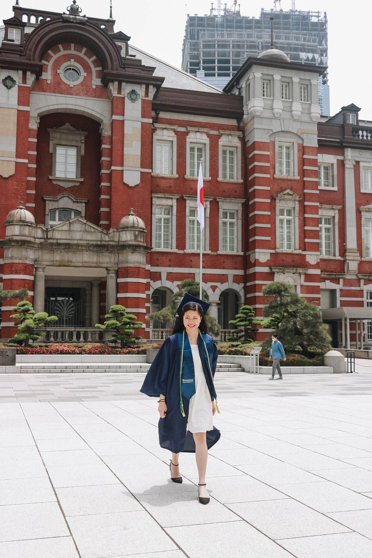 Graduate walking in academic gown in front of red brick Tokyo Station building.