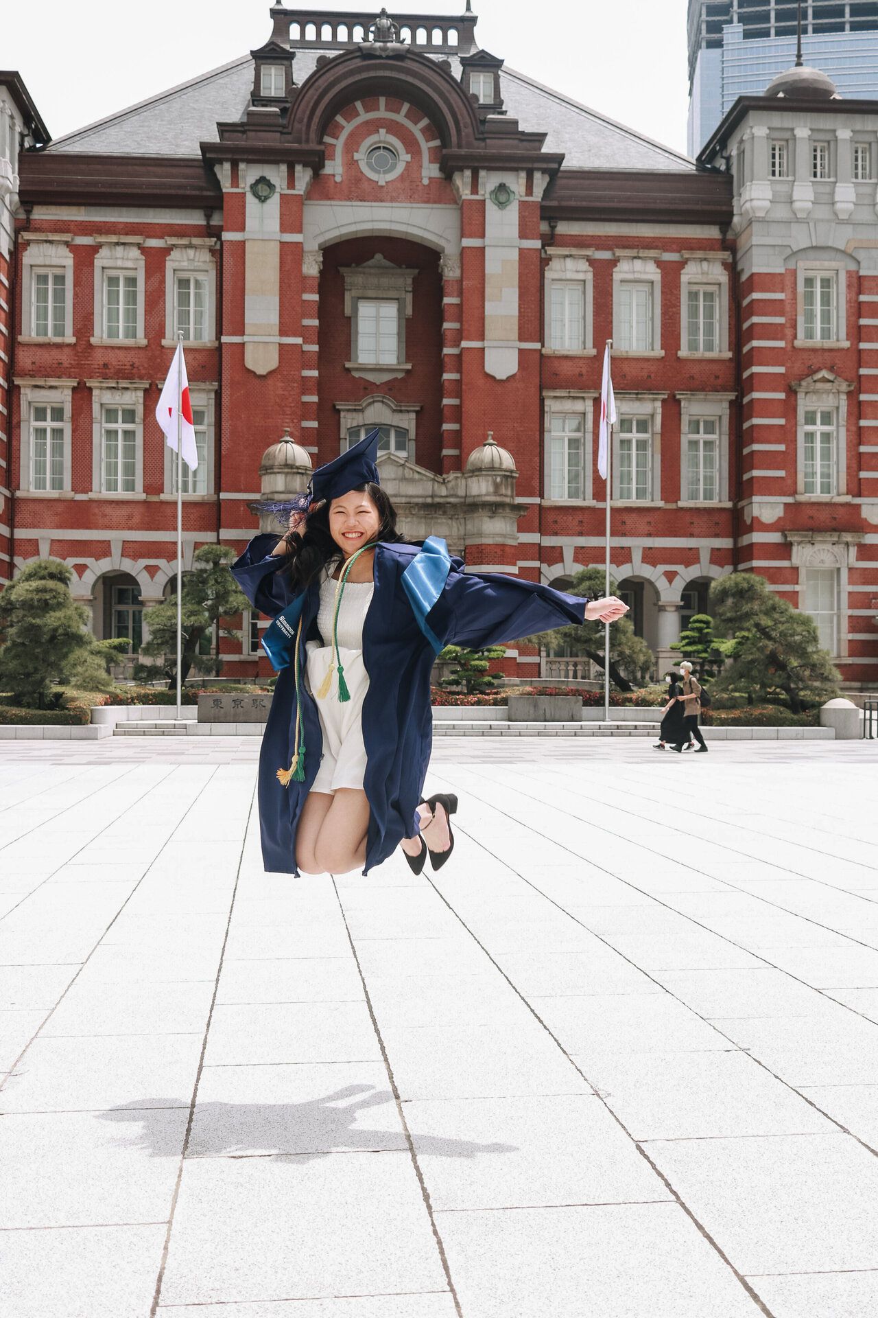 Graduate posing joyfully in front of historic Tokyo Station building with its iconic red brick architecture.