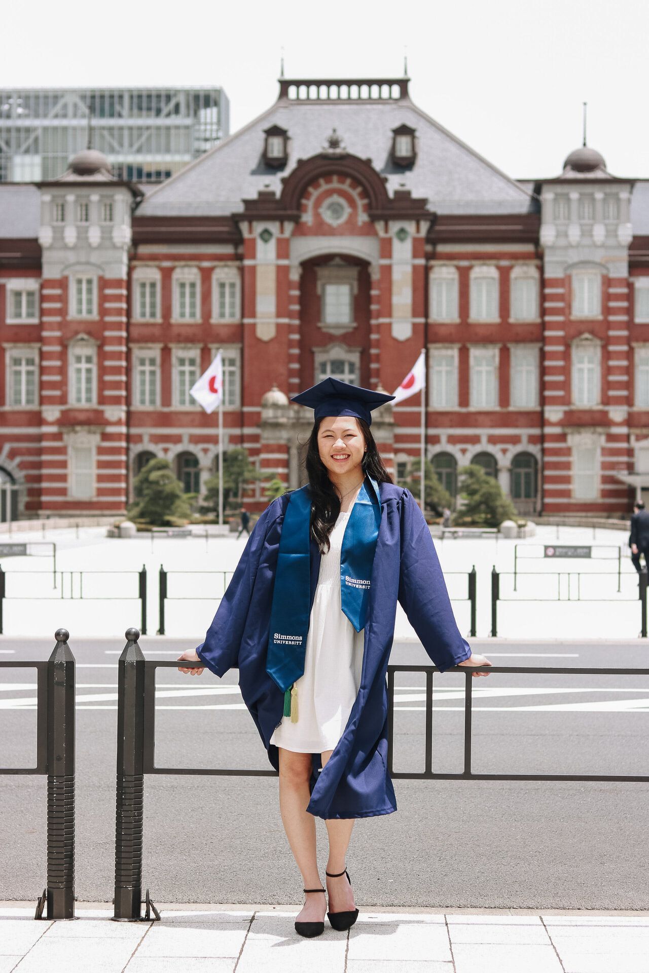 Graduate celebration photo in front of historic Tokyo Station with traditional red brick facade.