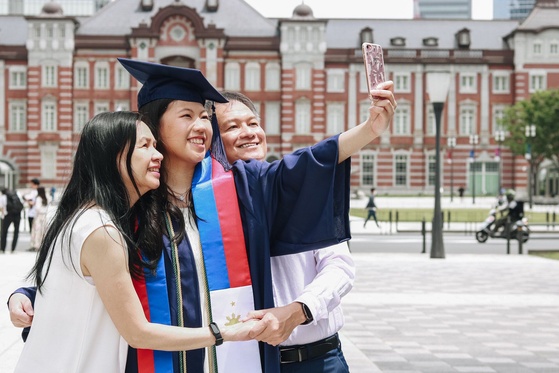 Group of graduates taking celebratory selfies in front of Tokyo Station.