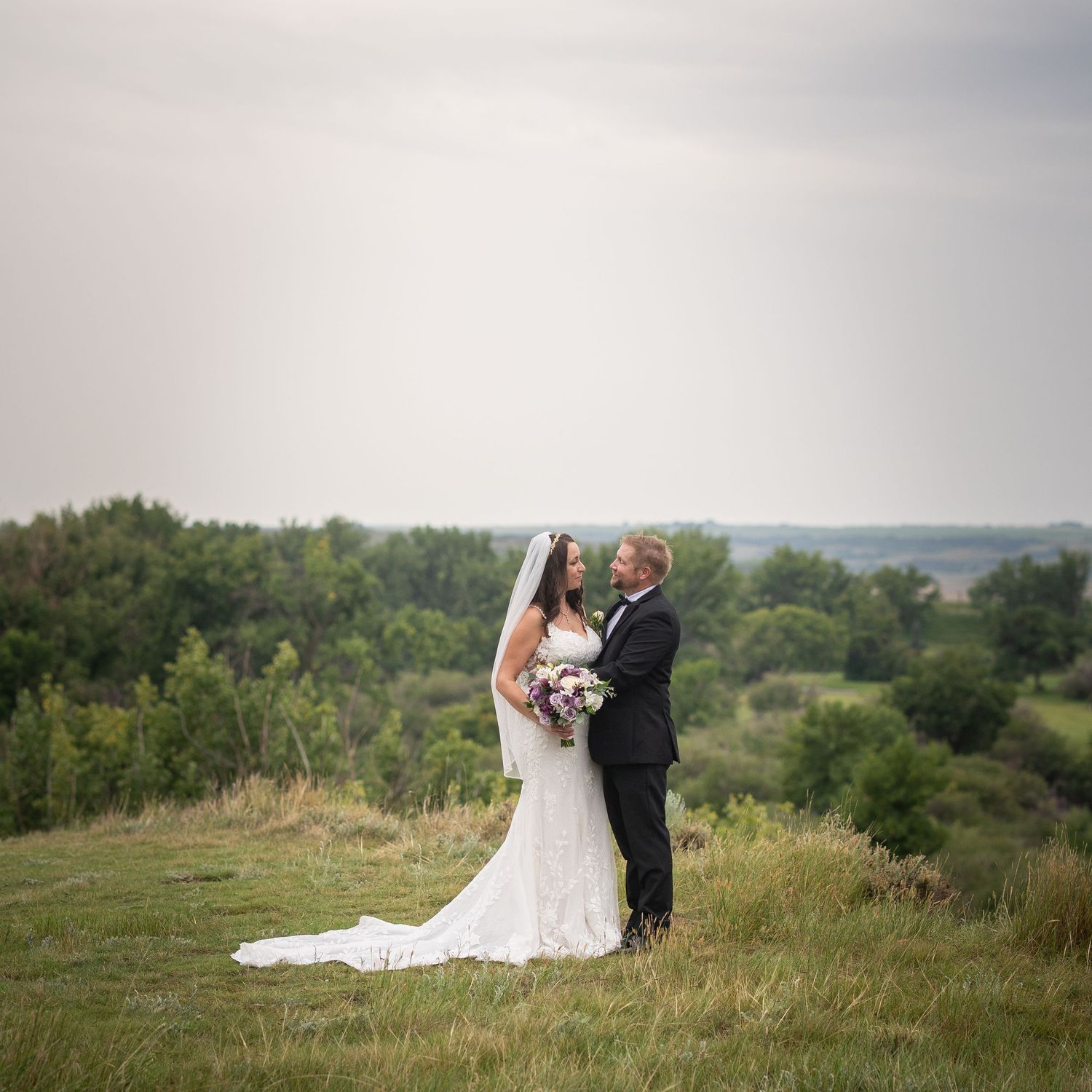 A couple shares an intimate moment on a hilltop overlooking a scenic green landscape on their wedding day.