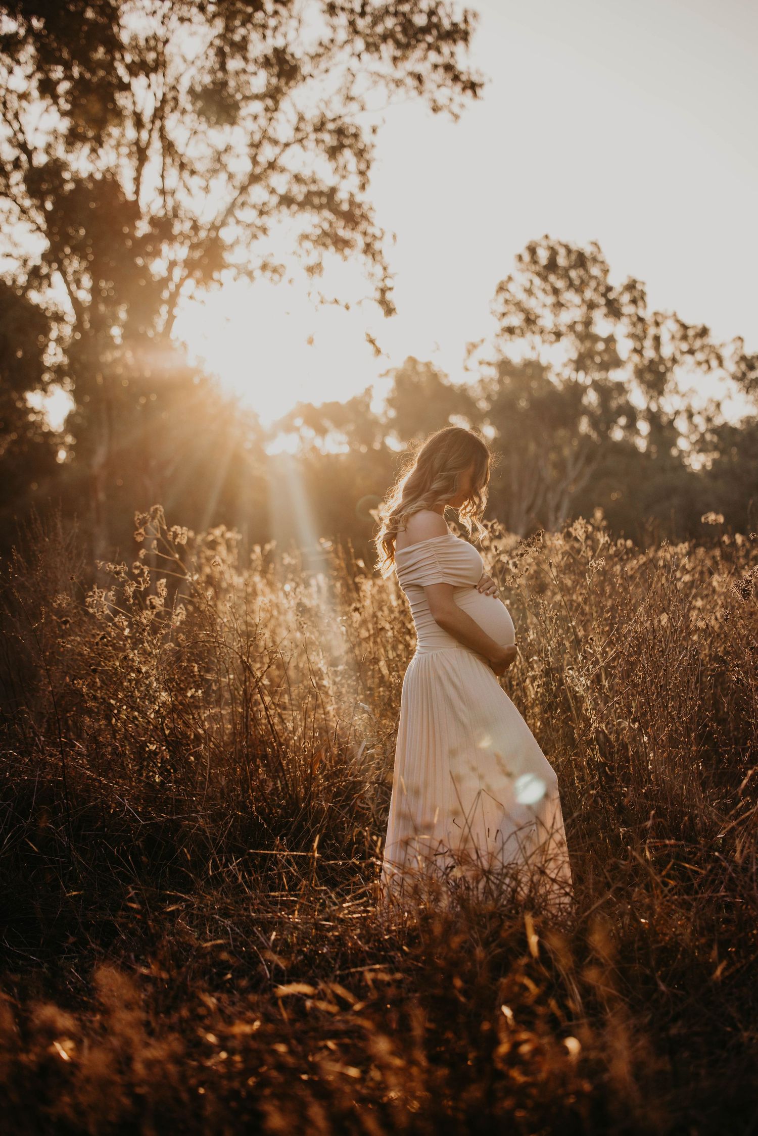 Ethereal portrait of a figure in white dress standing in golden sunlit field.
