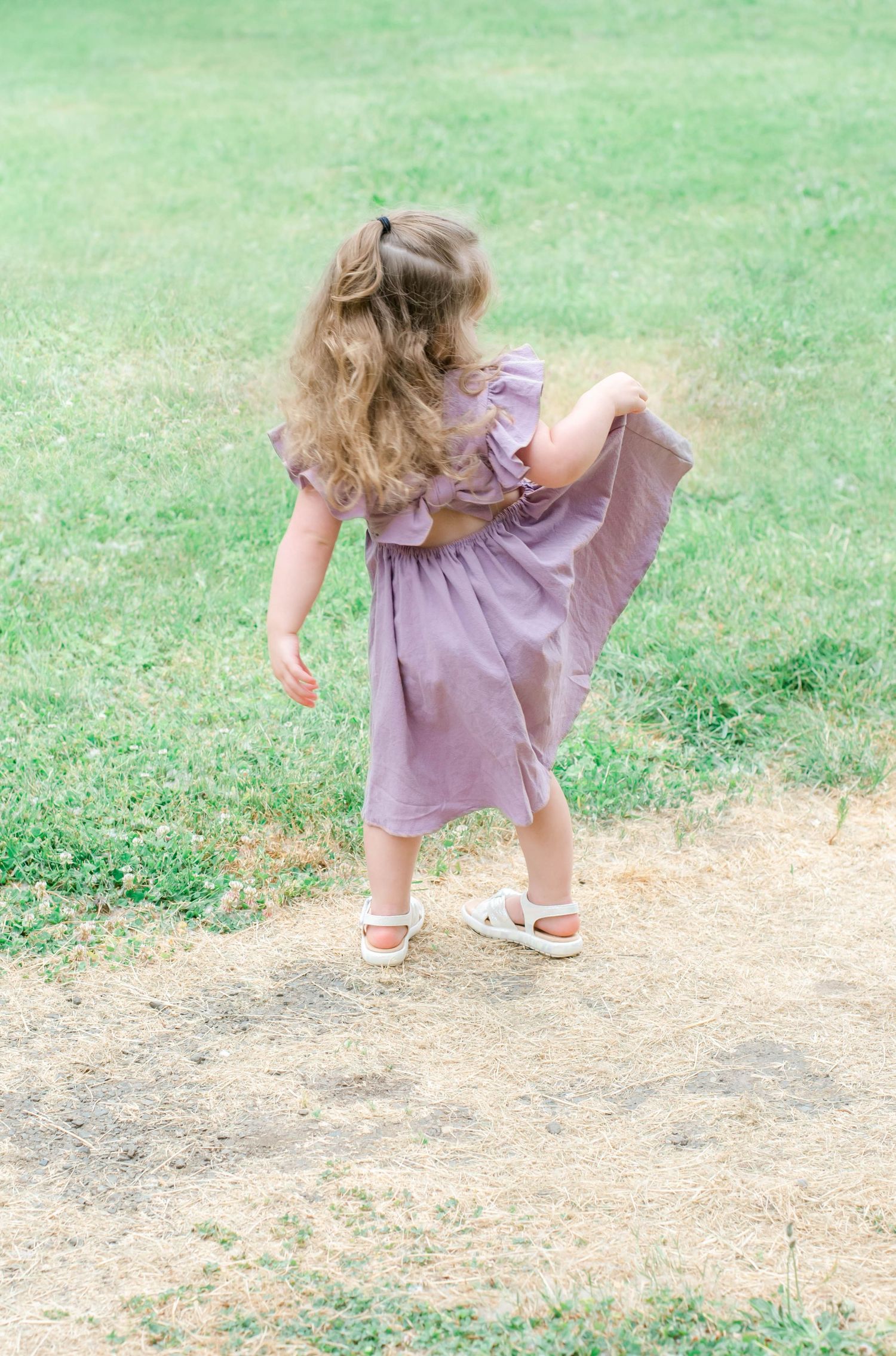 Child in purple dress bending down to explore something on dirt path.