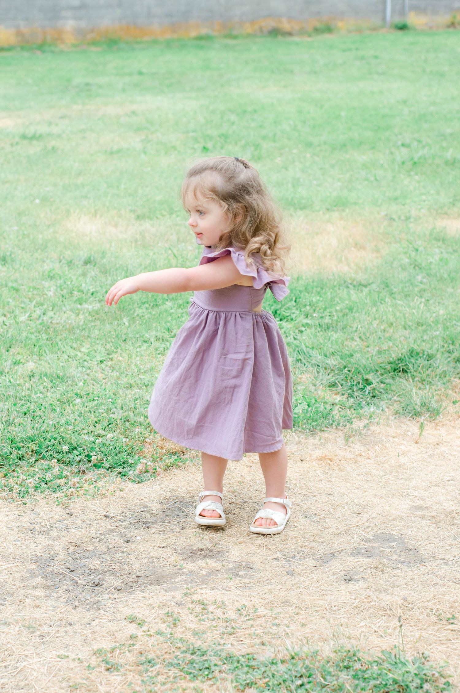 Small child in purple dress walking on dirt path through green grass field.