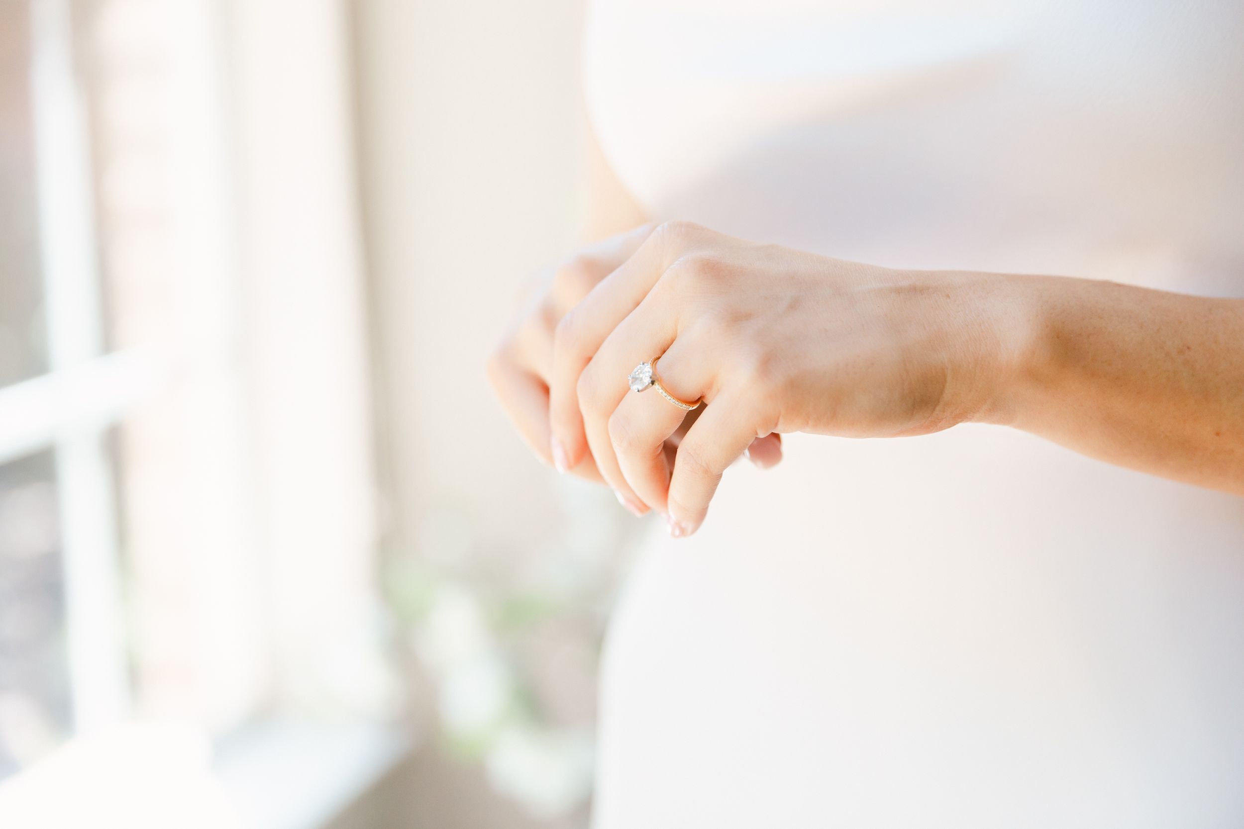 Close up of wedding details showing delicate white wedding dress and wedding ring against a soft light background.