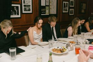 Wedding guests enjoying dinner at long table in traditional wood-paneled dining room.