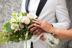 A close-up of hands holding a delicate white and green wedding bouquet against a formal suit.