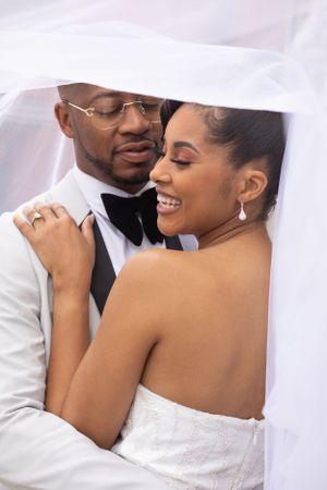 A romantic wedding portrait under a flowing white veil with elegant attire.