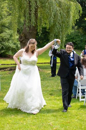 A joyful celebration under a weeping willow tree as a couple dances together on a lush green lawn during their outdoor wedding.