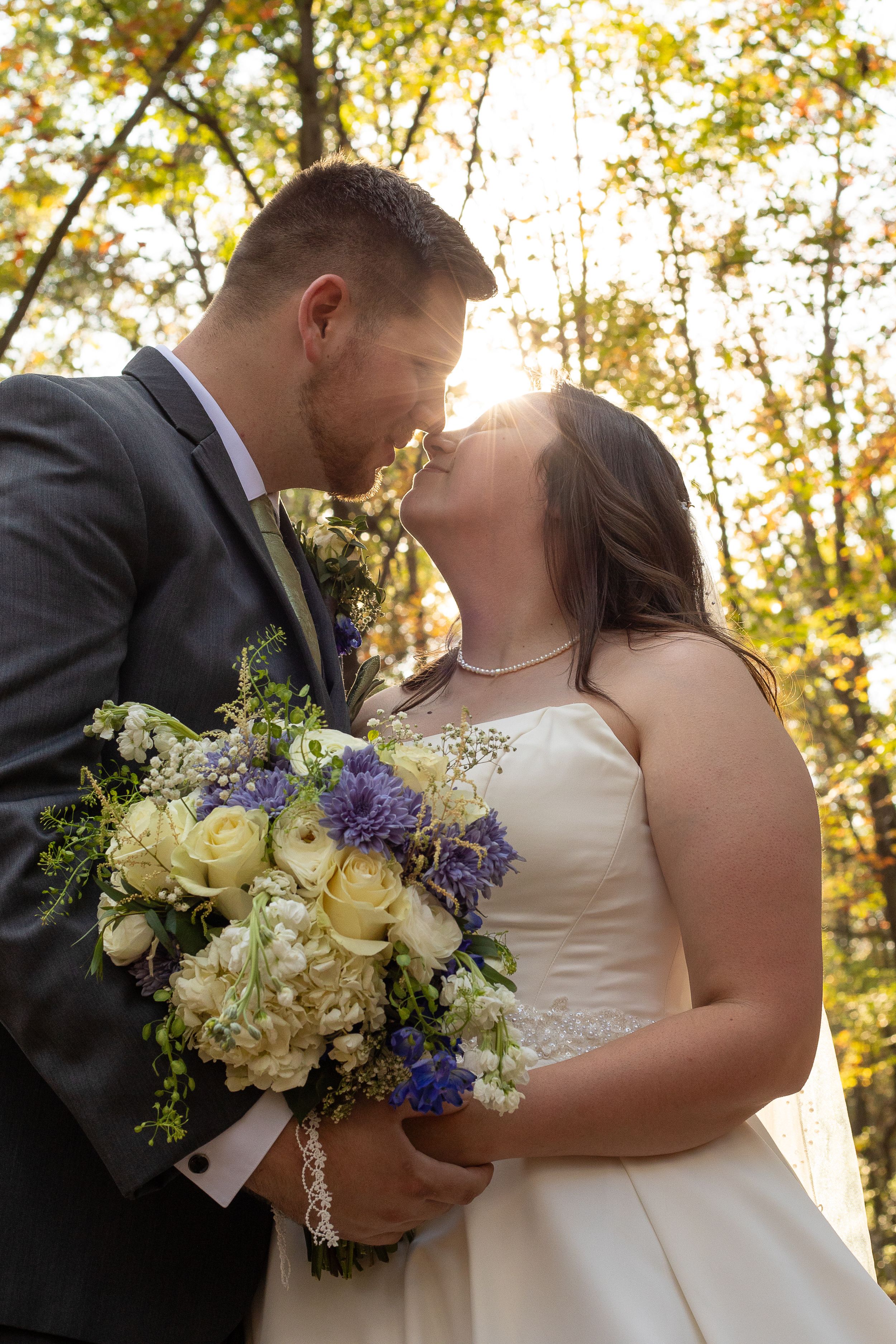 Bride and groom sharing romantic moment with sunlit autumn trees and bouquet.