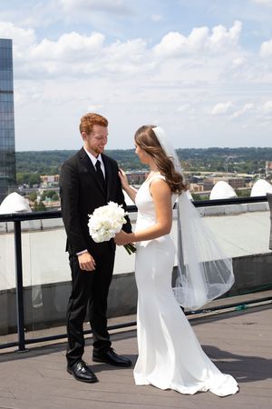 A couple shares their first look moment on a rooftop terrace overlooking a city skyline.