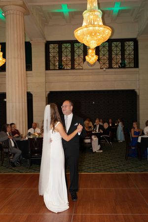 A couple dancing at a wedding reception under an elegant crystal chandelier in a grand ballroom.
