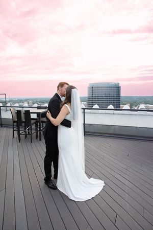 A couple shares an intimate moment on a rooftop deck with pink sunset skies and city views.