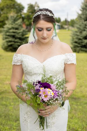 A delicate bridal bouquet with purple flowers held against a white wedding dress.