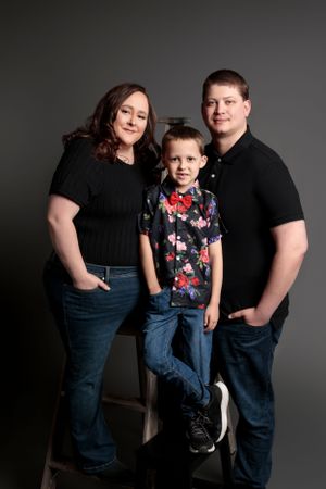 Studio portrait of a family of three wearing coordinating black and blue outfits against a dark background.