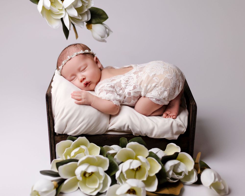 A newborn baby sleeping peacefully in a wooden basket adorned with soft white and yellow magnolia flowers.
