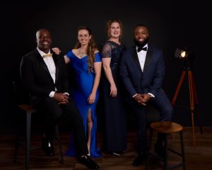 Two couples in formal evening attire pose elegantly for a studio portrait with vintage lighting equipment in the background.