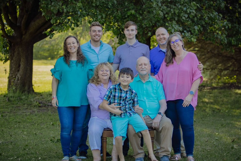 A group poses together outdoors in coordinated blue and pink outfits against a green natural background.