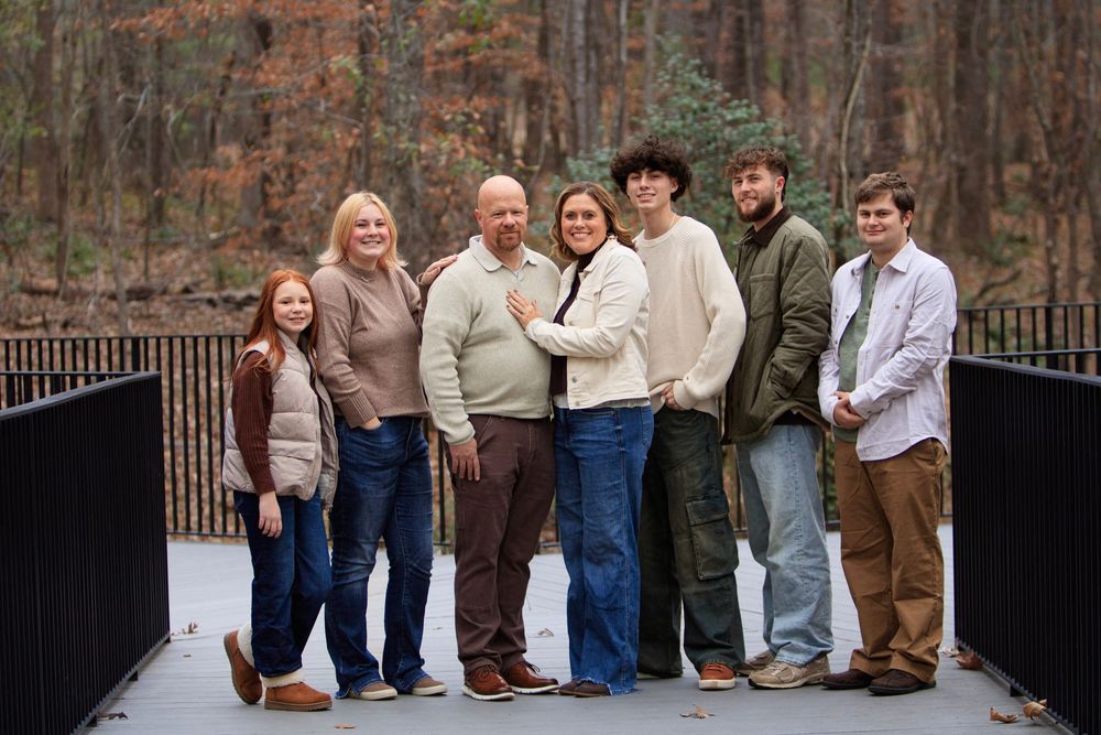 A group of people stand together on a wooden bridge in a forest during autumn.