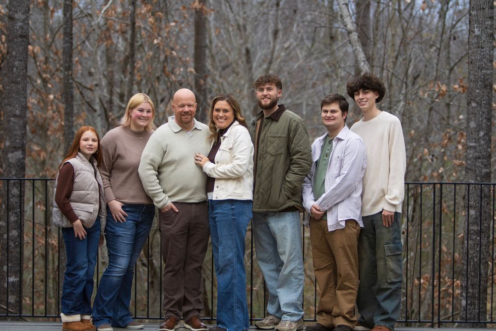 Family members in matching cream sweaters pose together on a wooden deck during an autumn photoshoot.