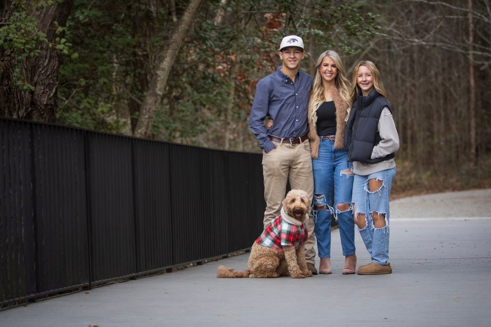 Family walks together on a paved path through a wooded area during autumn with their golden retriever dog.