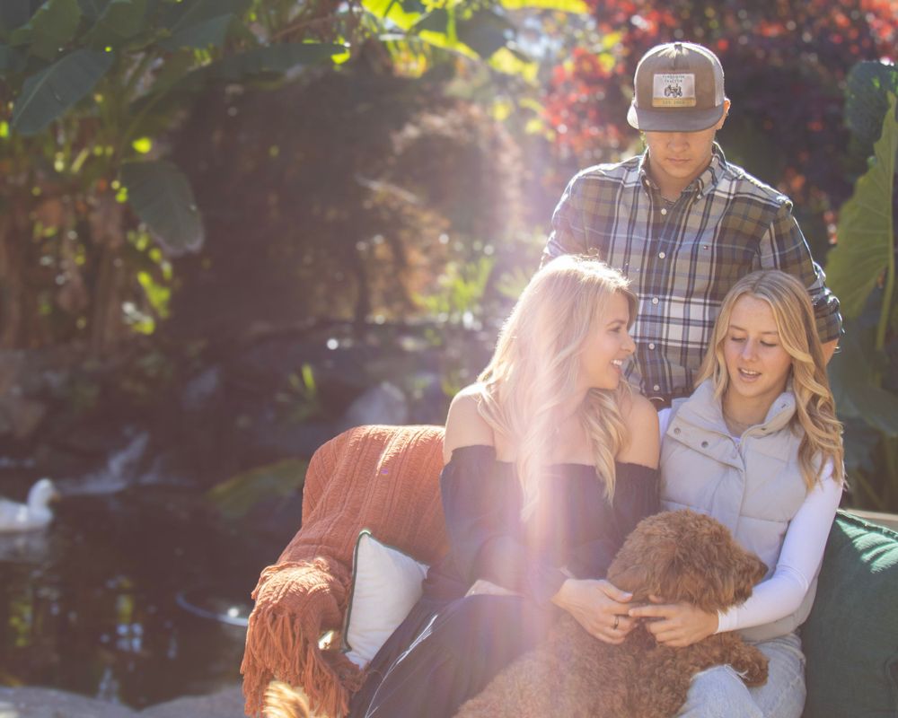Casual outdoor family photo session with sunlight and a curly-haired dog.