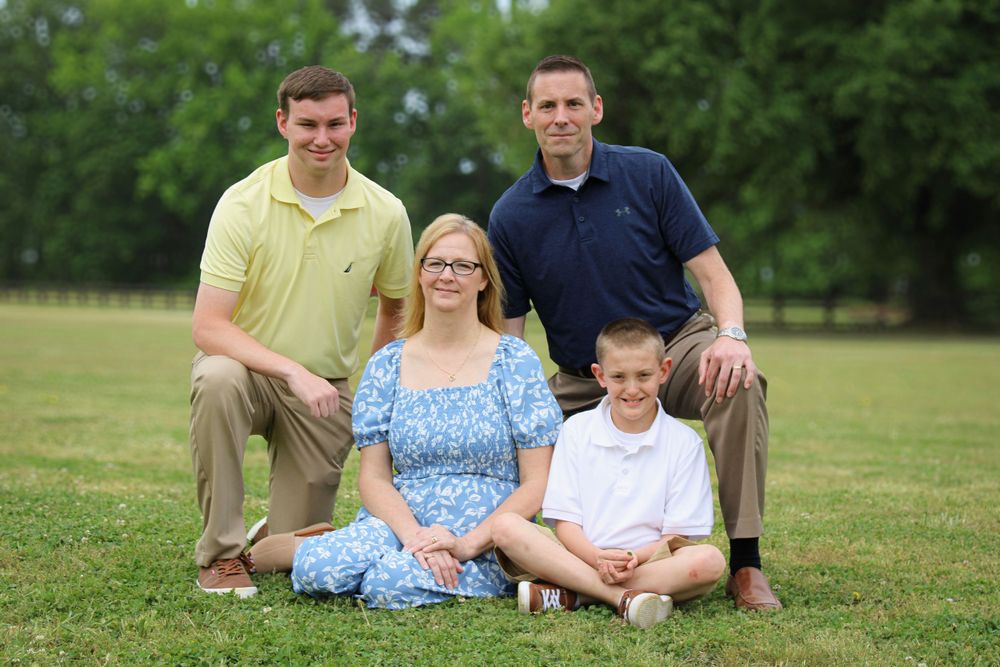 A family of four poses together on grass with trees in the background.