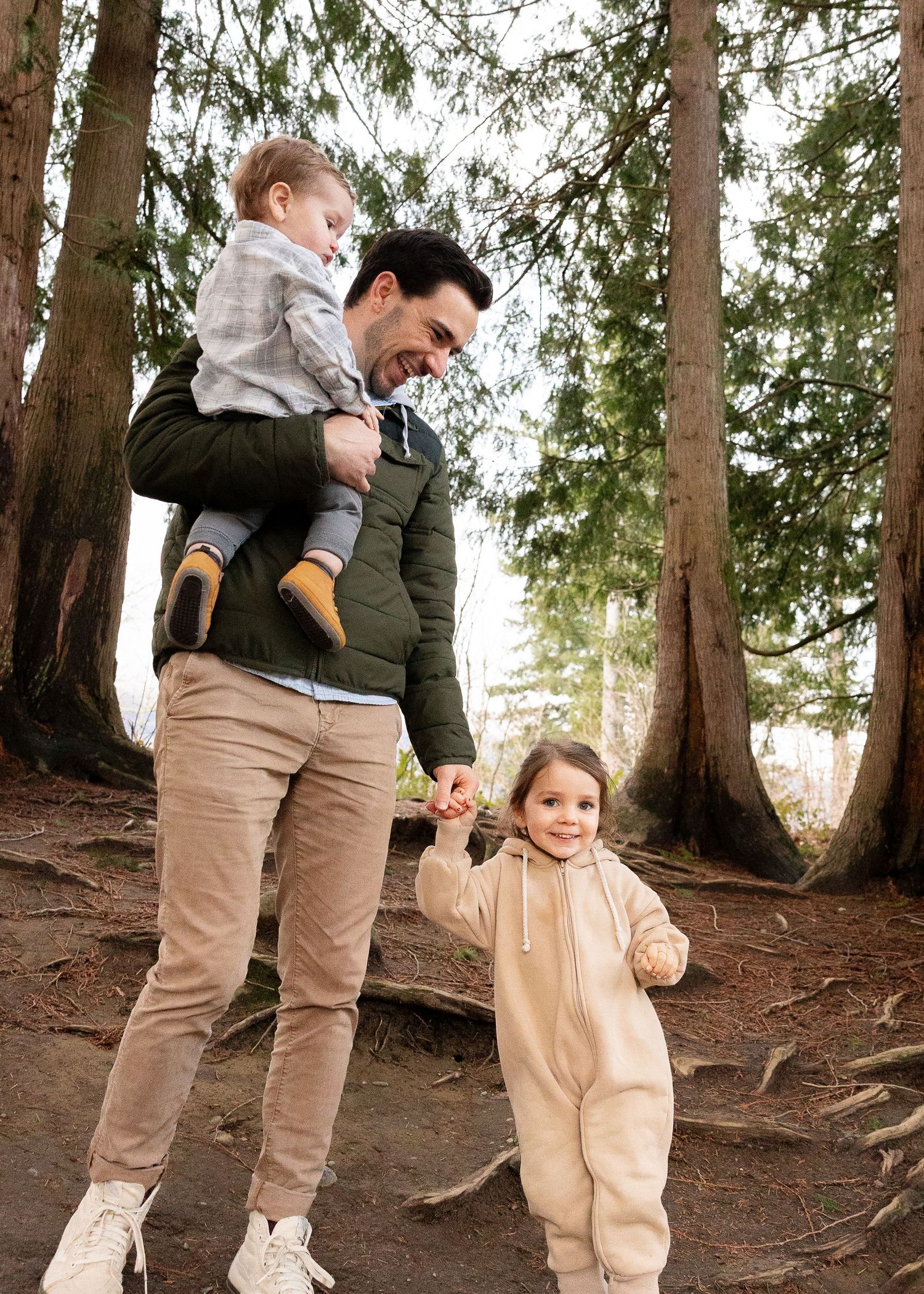 People walking through a wooded forest path surrounded by tall evergreen trees.