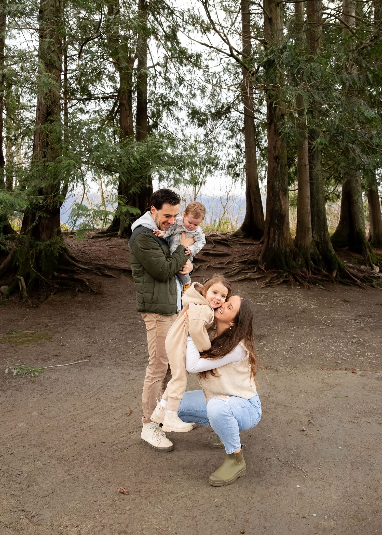 A family shares a joyful moment together on a forest trail surrounded by tall evergreen trees.