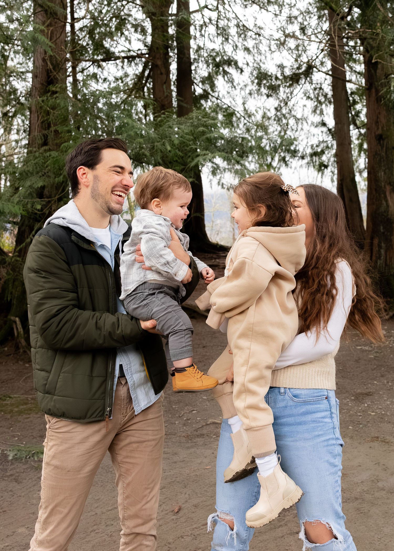 A family shares joyful moments together while standing among tall evergreen trees in a forest setting.