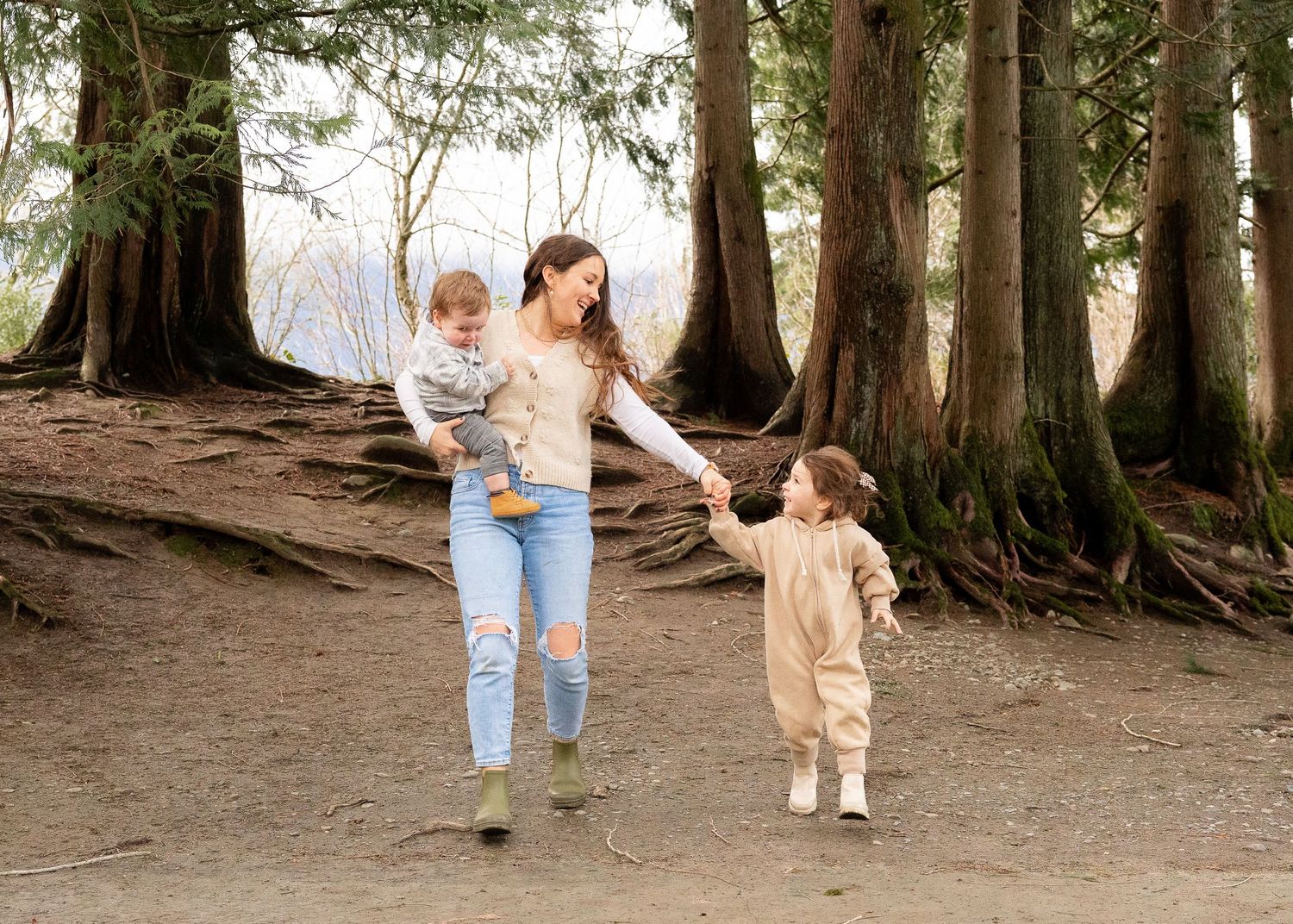 Two people walk along a dirt path between tall trees in a forest park.