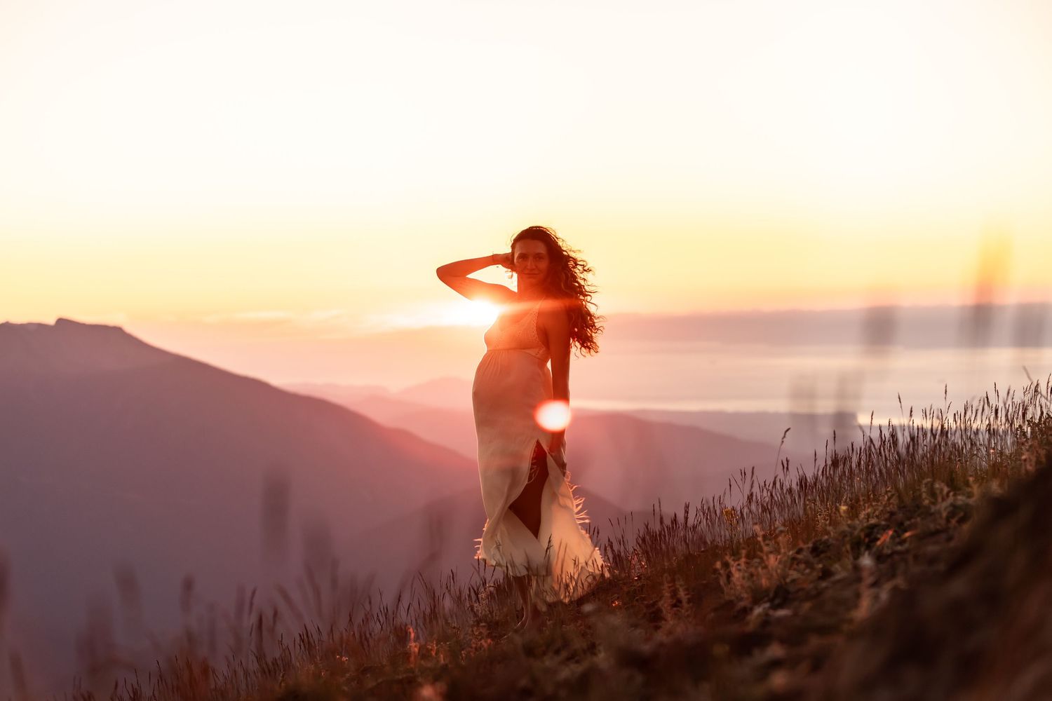 Silhouette of a person in flowing dress against mountain sunset.