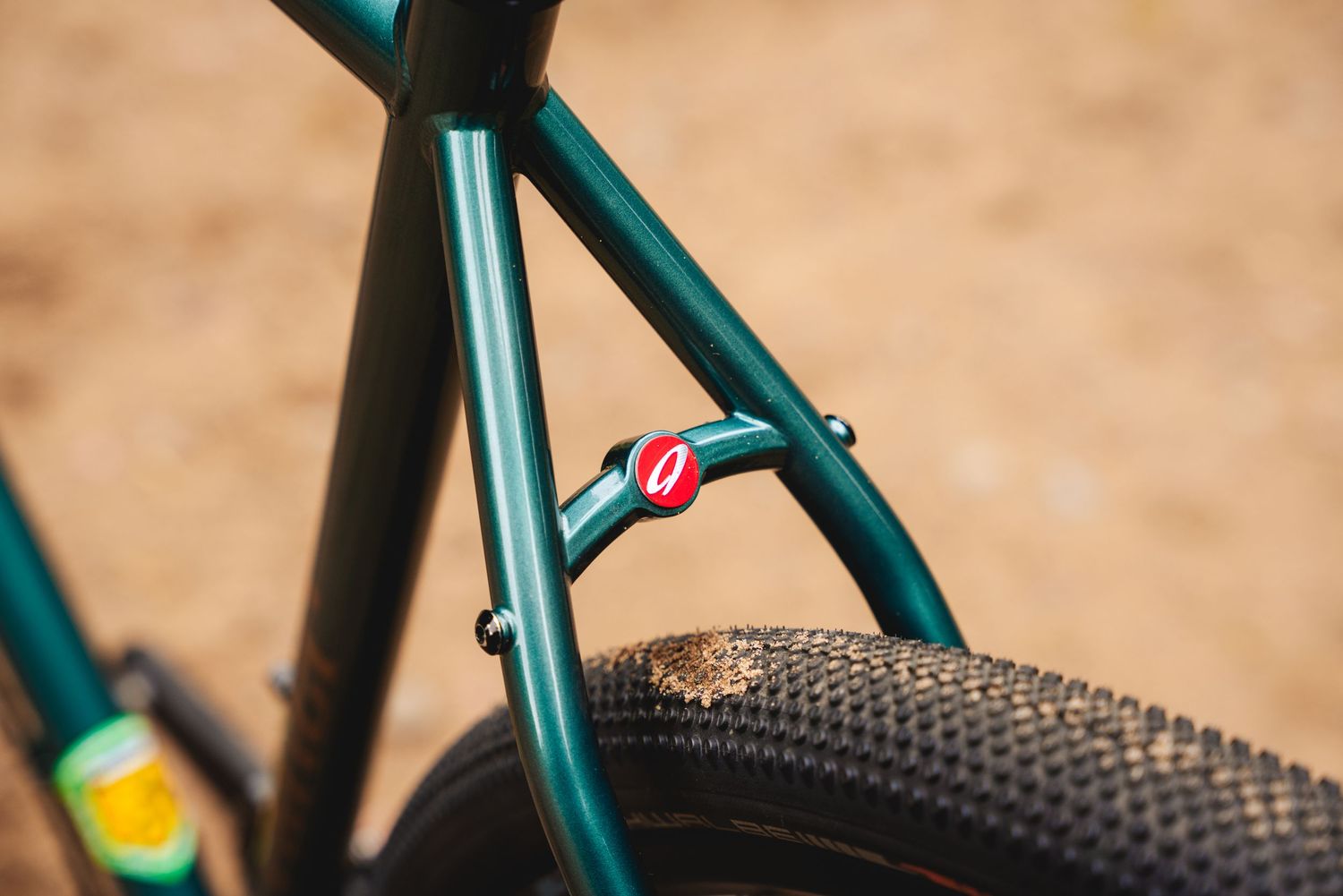 Close-up detail of a metallic teal bicycle frame with a knobby tire and small red accent component.