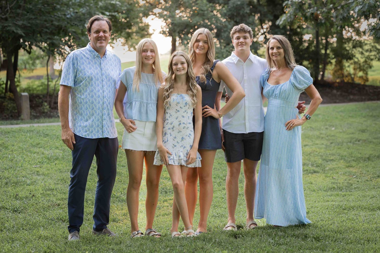 Group photo of people wearing coordinated blue and white outfits outdoors. Family session at OPPD Arboretum