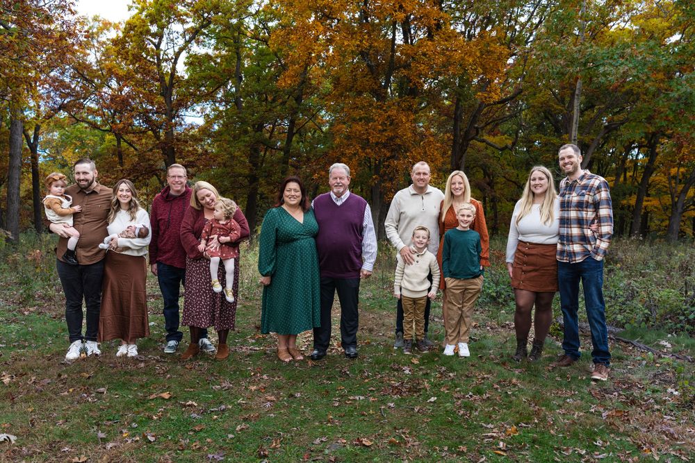 Large family posing outdoors in autumn forest wearing coordinated earth-tone outfits during fall foliage season.