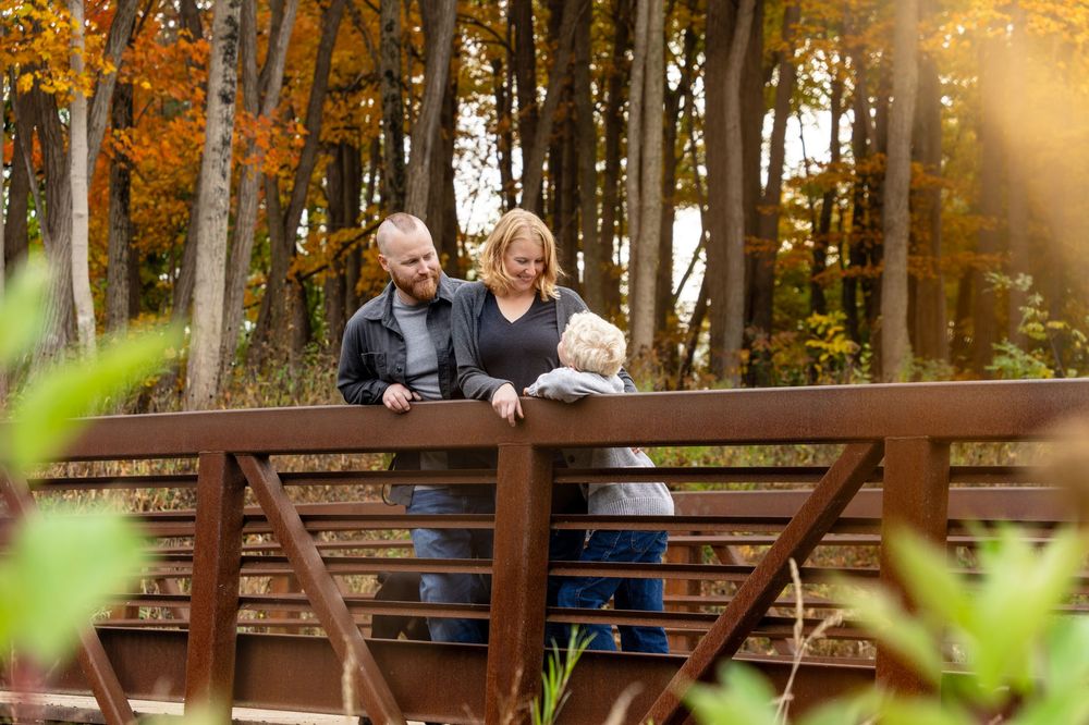 Family of three enjoying autumn foliage on a wooden bridge in a colorful fall forest setting.