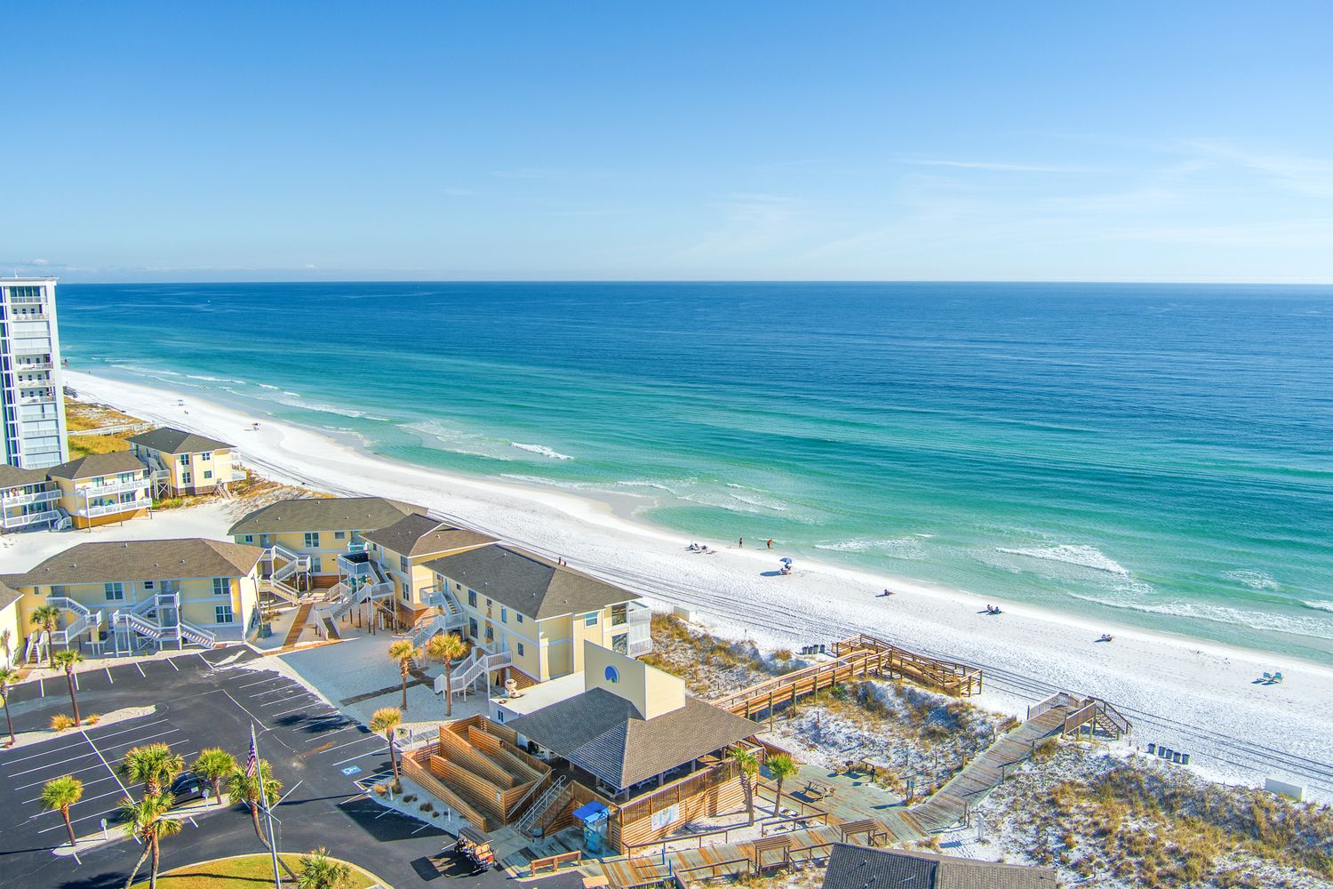 Aerial view of turquoise ocean waves crashing on white sand beach with palm trees and beachfront buildings in Florida.