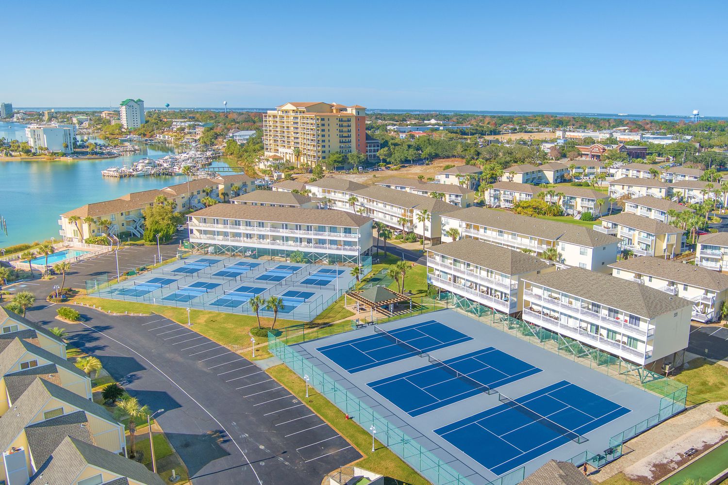 Aerial view of pickleball and tennis courts at beachside resort complex with condominiums and waterfront views.