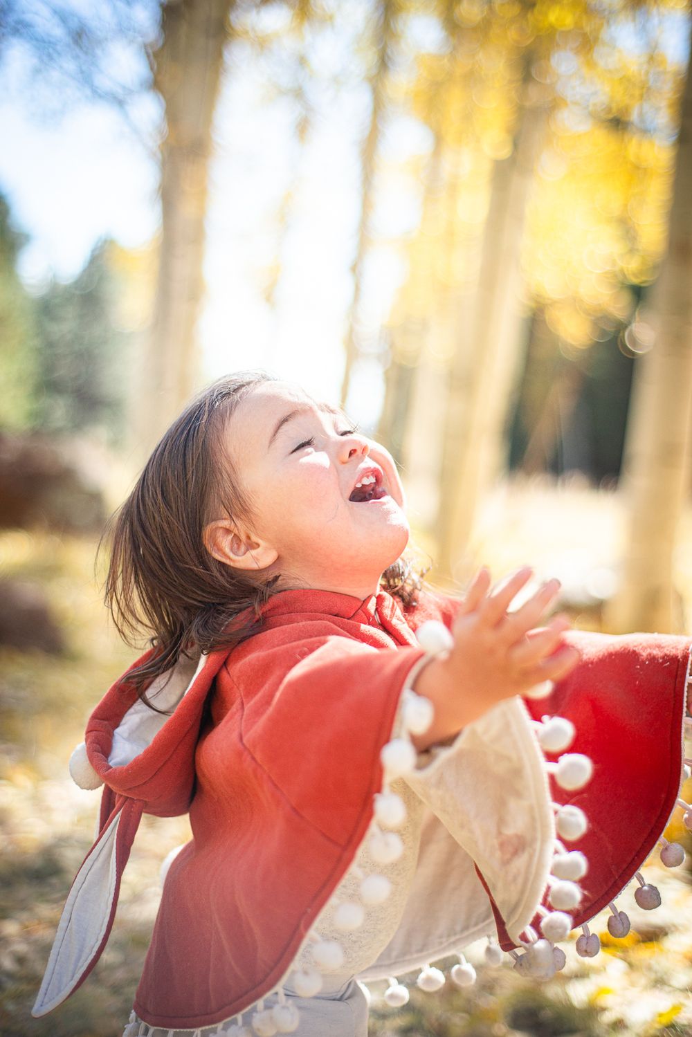 Child in red coat laughing joyfully among golden aspen trees.