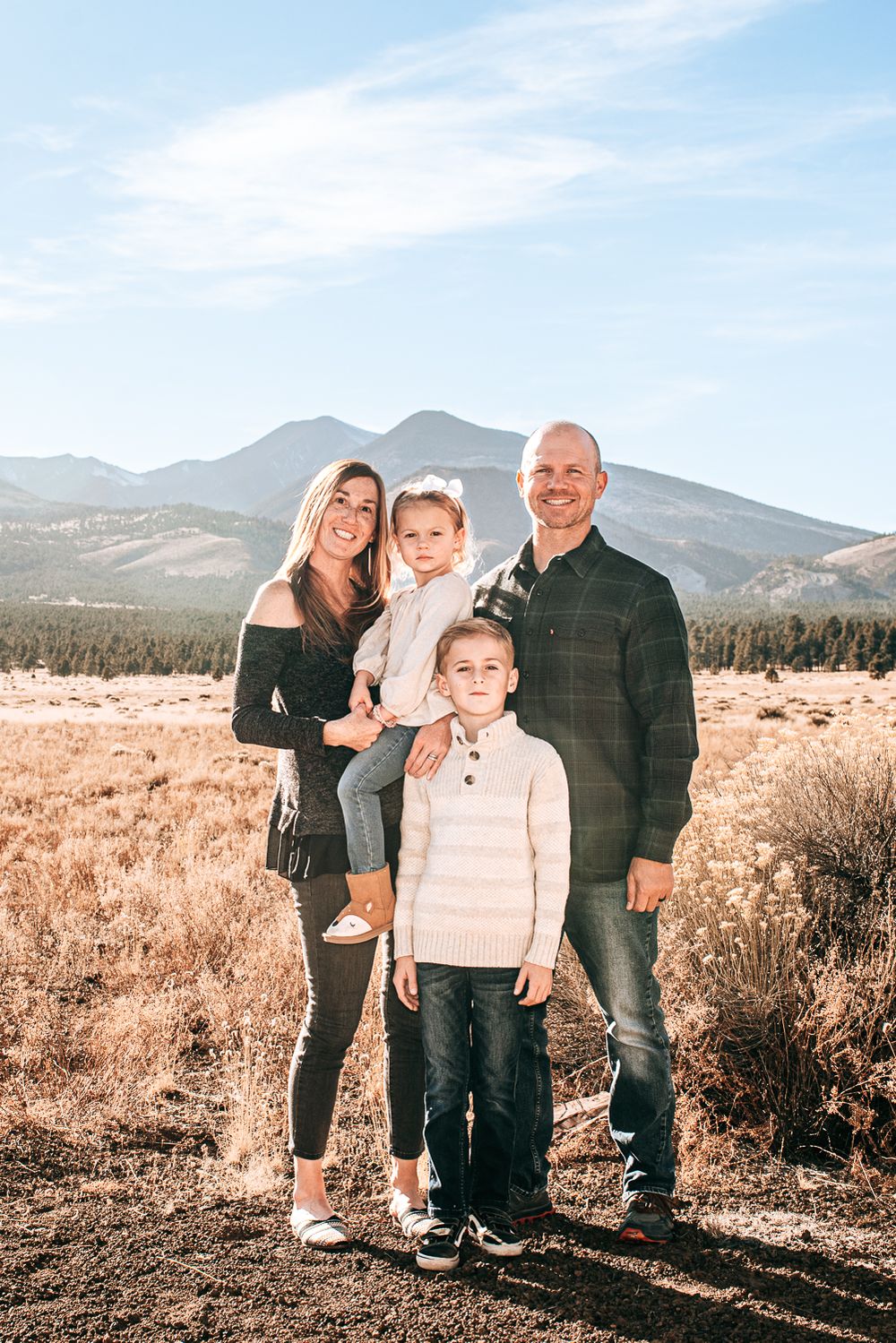Family of four poses for portrait with mountain landscape in background.