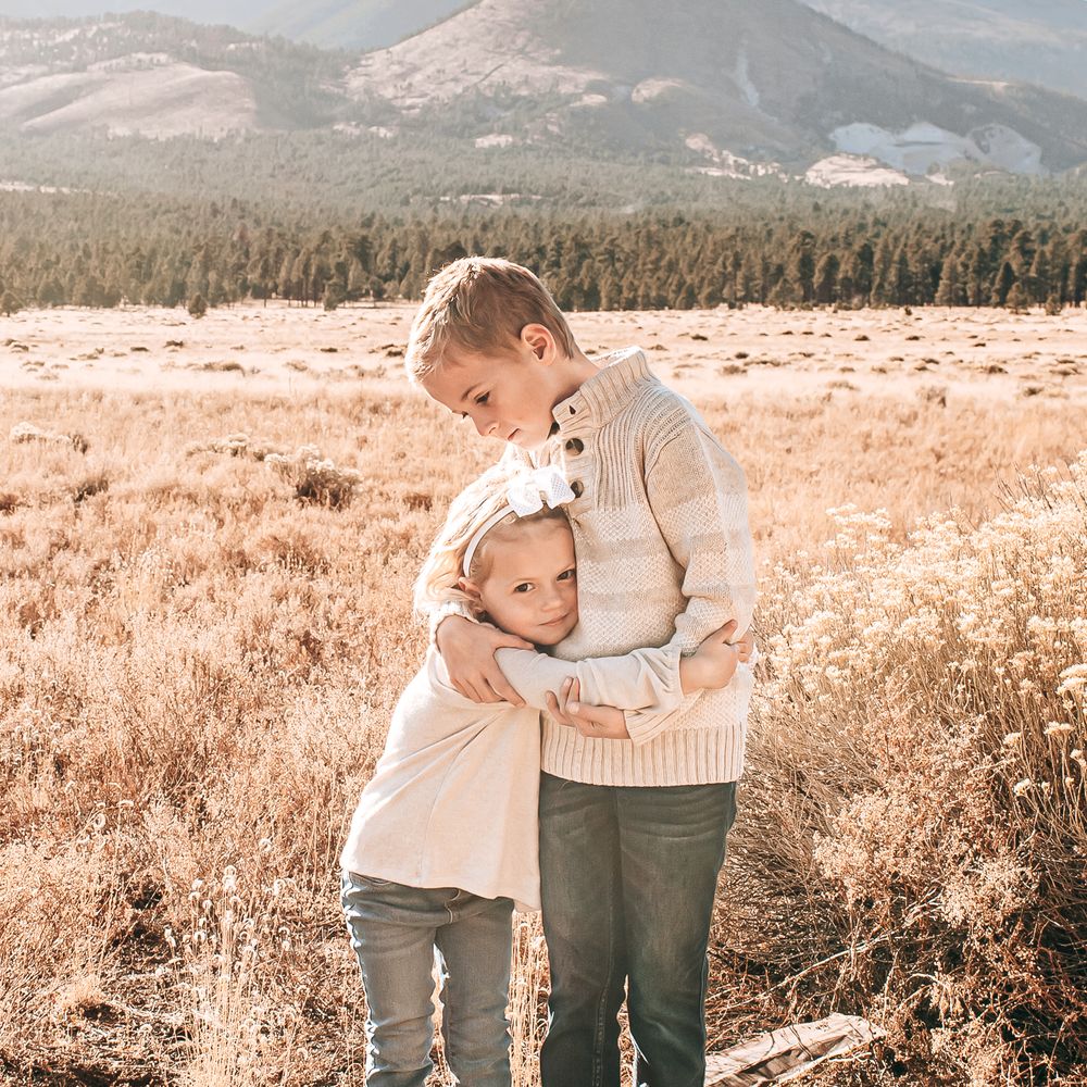 Two children sharing a tender moment in a sunny autumn field with mountains in background.