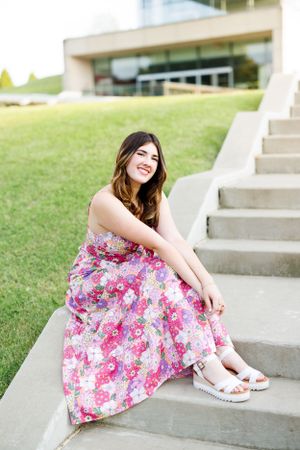 Person in pink floral dress sitting on concrete steps outdoors.
