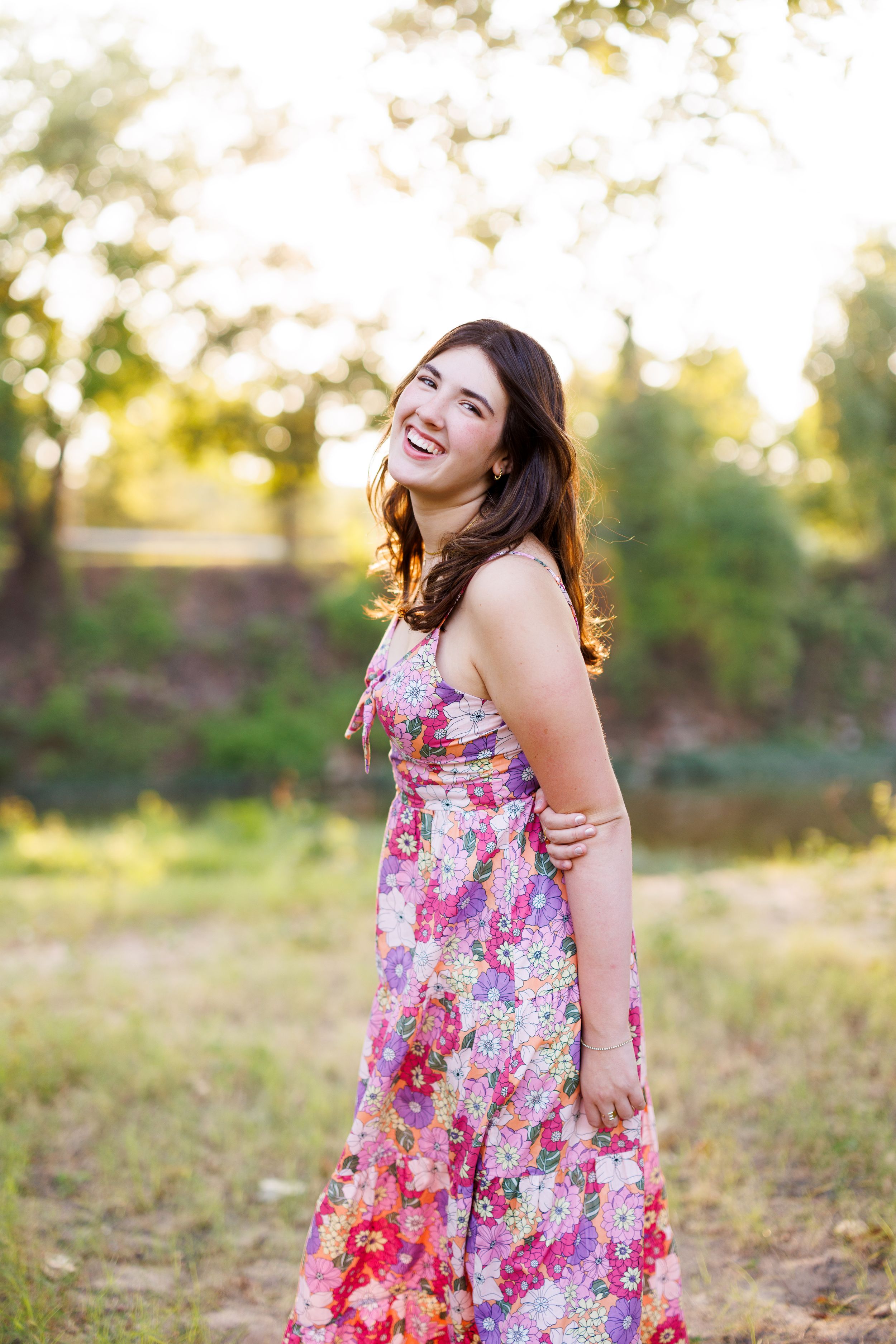 A floral summer dress is worn in a sunlit outdoor setting during golden hour.