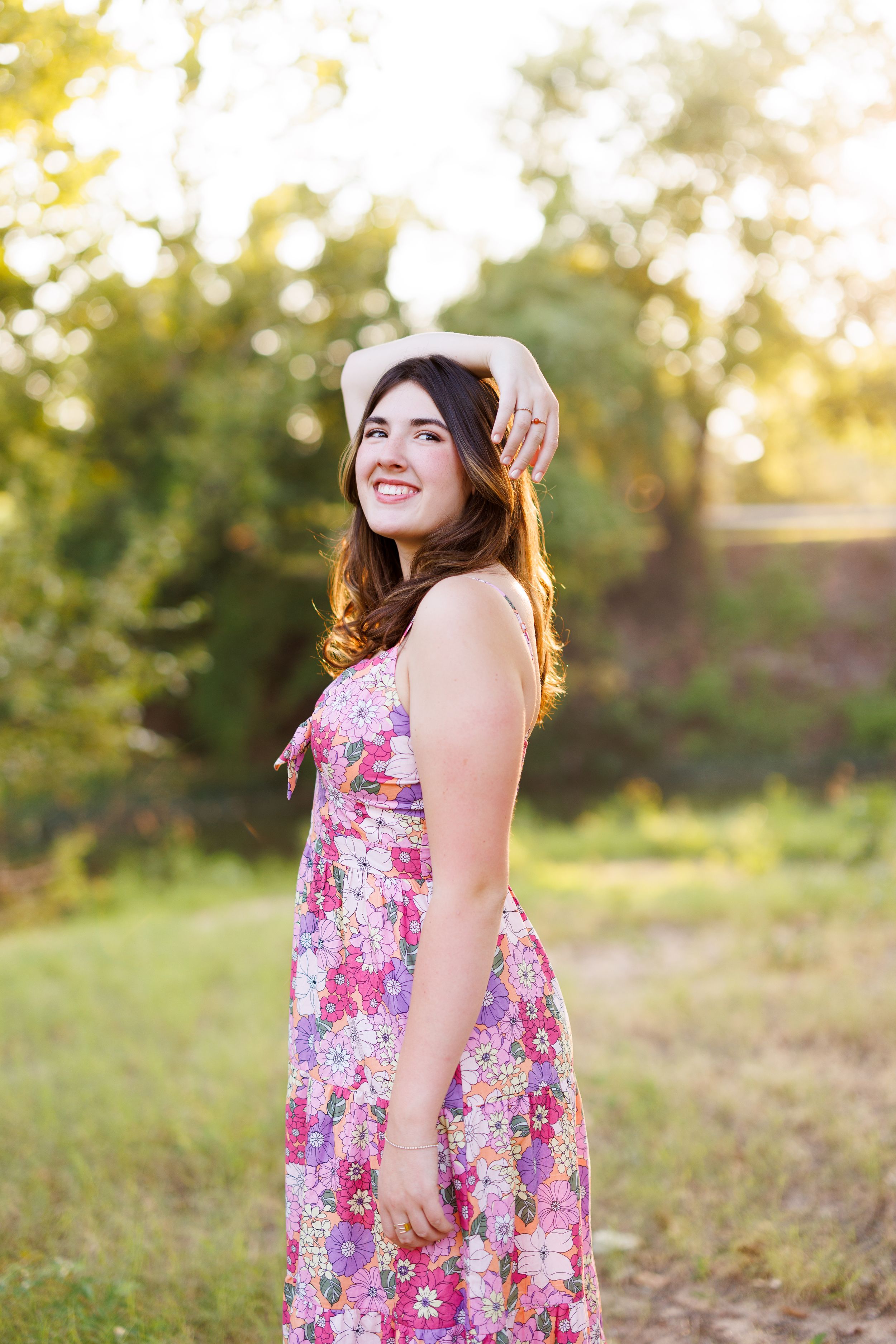 A floral dress is showcased against a natural outdoor backdrop with warm lighting.
