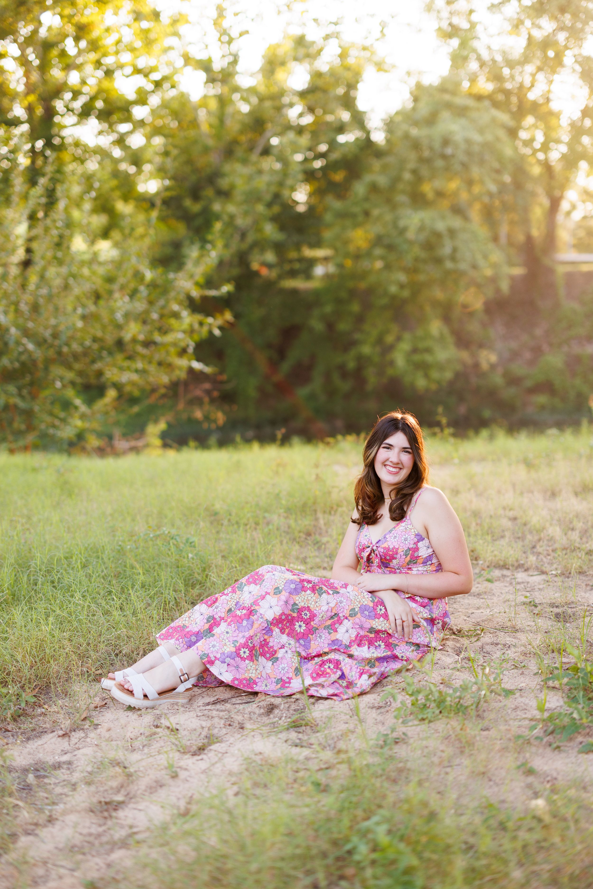 A pink floral dress is worn while sitting in a grassy field at sunset.