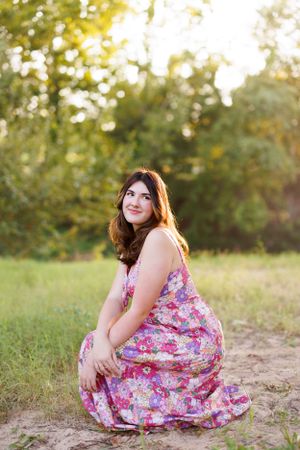 A flowing floral dress is modeled in a natural outdoor setting with golden sunlight.