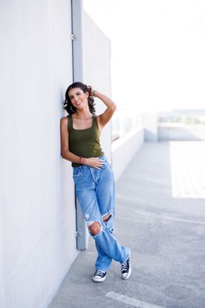 Casual portrait against white wall wearing olive tank top and distressed jeans.