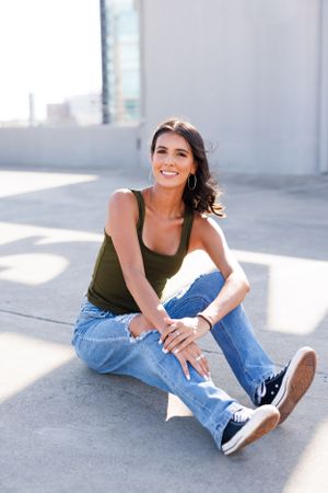 Relaxed urban style portrait with olive tank top and ripped jeans on concrete floor.