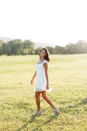 Woman in white summer dress walking through golden meadow at sunset.