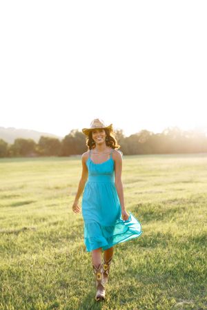 Figure in bright blue dress runs through a grassy field at sunset.